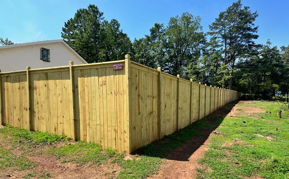 New wooden privacy fence installed by Spectrum Fence, stretching across a grassy yard with trees in the background